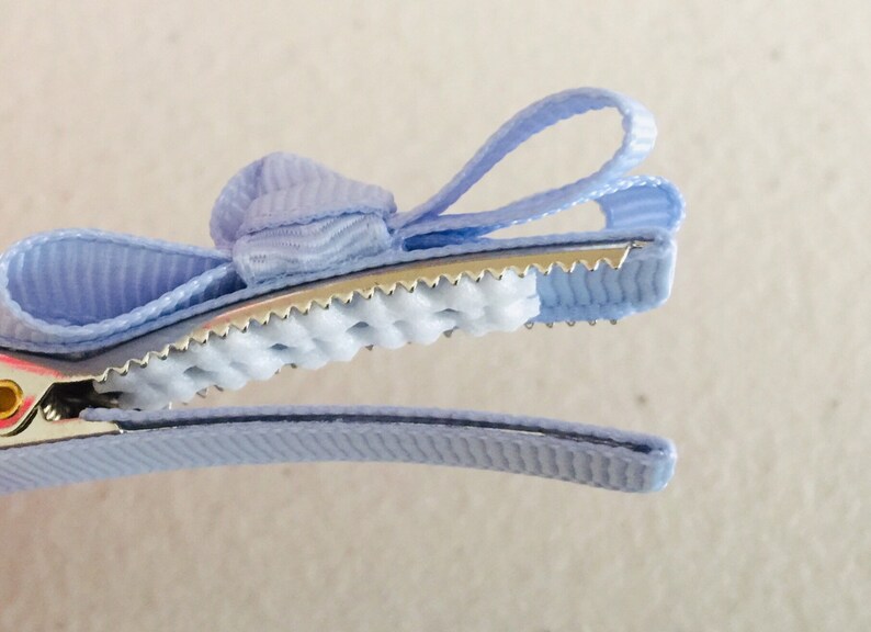 May include: A light blue hair clip with a bow. The clip has a textured grip and a metal spring.