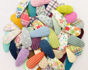 May include: A collection of colorful fabric-covered snap hair clips in various patterns and textures. The clips feature floral, polka dot, striped, and plaid designs in shades of pink, blue, yellow, and green. These hair accessories are ideal for adding a touch of style.
