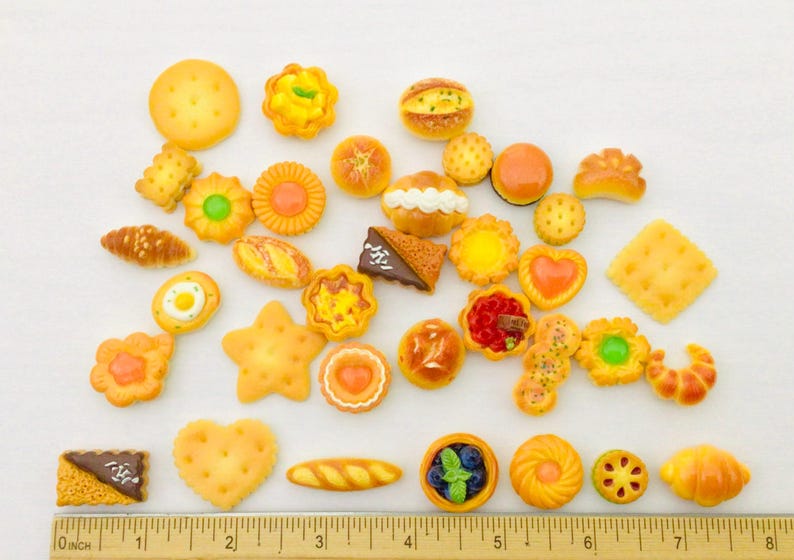 May include: A selection of miniature baked goods, including cookies, pastries, and bread, in various shapes and sizes. The assortment features a star-shaped cookie, a heart-shaped cookie, and a croissant. A ruler is at the bottom, measuring in inches (approx. 2.54 cm).