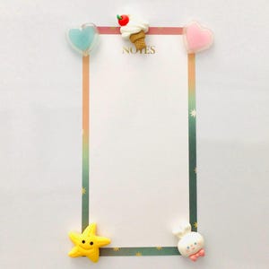Peut inclure: Un bloc-notes blanc avec une bordure color&eacute;e et le mot "NOTES" en haut. Orn&eacute; d'&eacute;l&eacute;ments d&eacute;coratifs : un c&oelig;ur bleu, une glace, un c&oelig;ur rose, une &eacute;toile de mer jaune et un personnage blanc avec un n&oelig;ud rose.