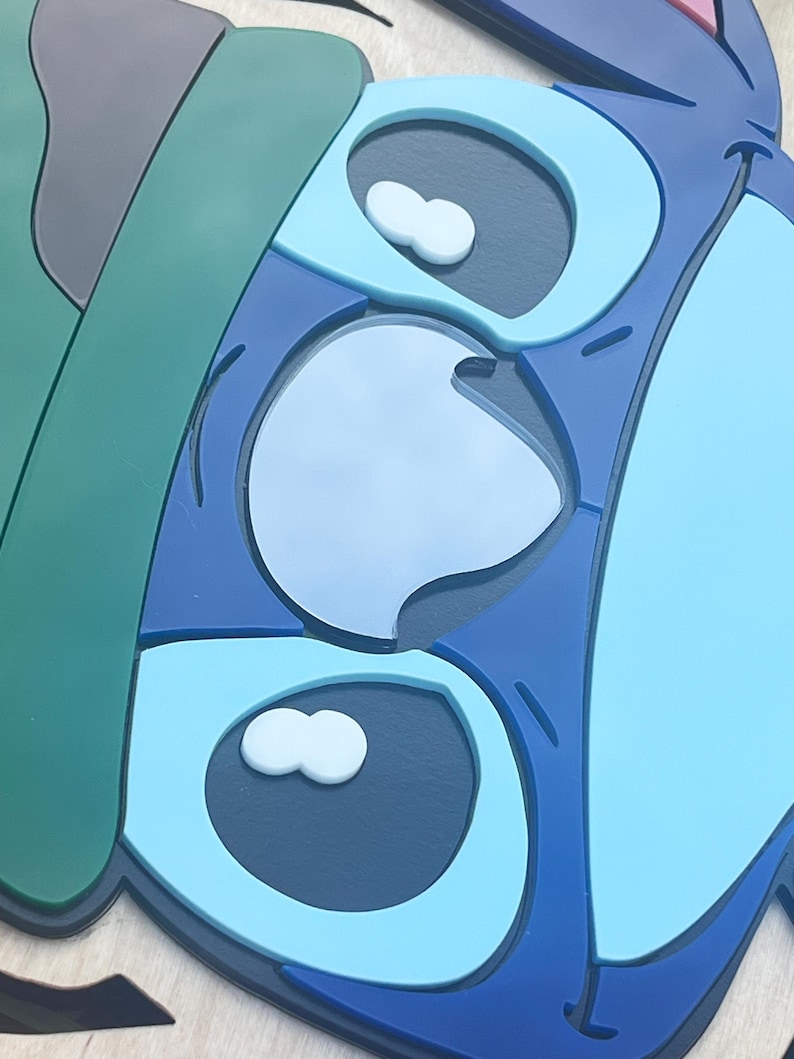 May include: A close-up of a blue, green, and gray cartoon character face. The character has large eyes with white accents and a light blue nose. The design is layered with different shades of blue.