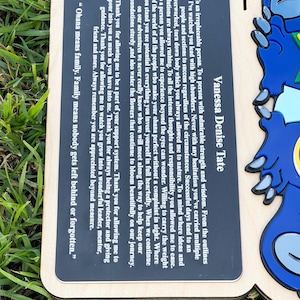 May include: Wooden plaque with a black rectangular insert featuring the text "Vanessa Denise Tate" and a heartfelt message about family and appreciation. The plaque has a blue character design on the right side.