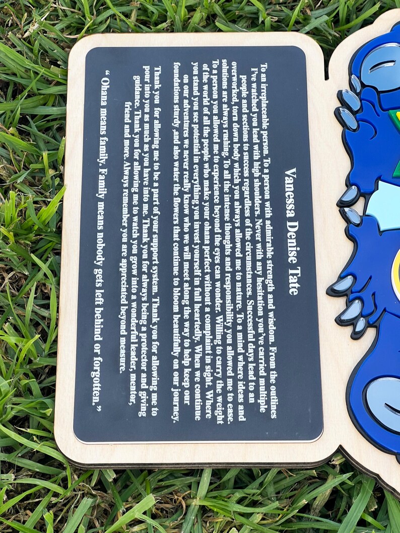 May include: Wooden plaque with a black rectangular insert featuring the text "Vanessa Denise Tate" and a heartfelt message about family and appreciation. The plaque has a blue character design on the right side.