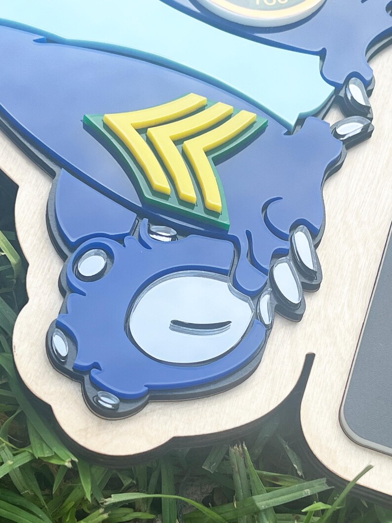 May include: A layered wooden plaque featuring a blue and light blue design with yellow and green accents. The plaque has a unique shape and a glossy finish. The design includes a stylized emblem.
