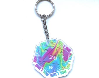 May include: A keychain featuring a holographic D20 die with the number 20 prominently displayed. The die is multi-colored with the word "ROLLING" around the edges. The keychain has a silver chain and ring.
