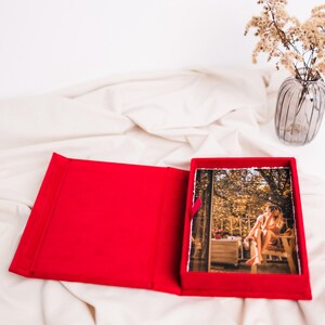 Puede incluir: Un álbum de fotos de terciopelo rojo con una foto de una persona sentada en un porche con árboles en el fondo.