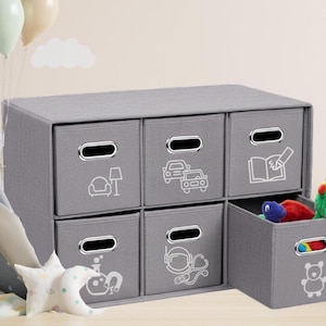 May include: A gray fabric storage organizer featuring six rectangular bins with silver-toned handles. Each bin displays a white line-art icon, including a chair, cars, a book, a beaker, a stethoscope, and a teddy bear, with one bin pulled outward.