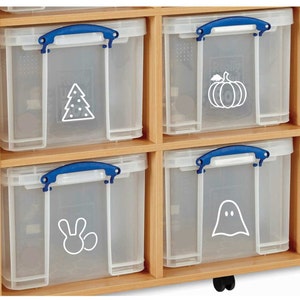 Puede incluir: Seis cajas de almacenamiento de plástico transparente con asas azules y pegatinas blancas con temática navideña. Las cajas están dispuestas en dos filas de tres y están sobre un estante de madera.