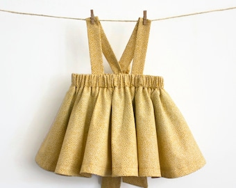 May include: A yellow skirt with white polka dots and adjustable straps. The skirt has a gathered waist and a bow at the back.