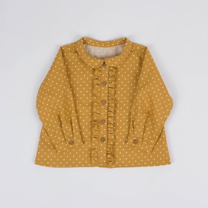 以下が含まれることがあります： 白い水玉模様のマスタードイエローのロングスリーブシャツ。フリル付きの前身頃で、ピーターパンカラーとボタン留めです。