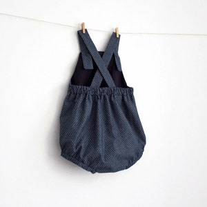 May include: A blue and black polka dot baby romper with a criss-cross strap back.