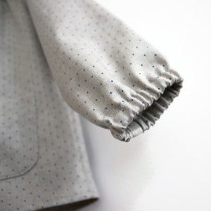 May include: Close-up of a grey and white polka dot fabric with a blue elastic band at the end of the sleeve.