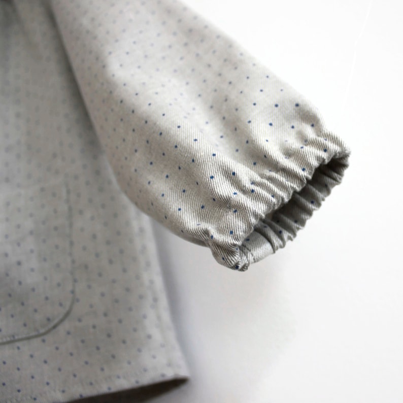 May include: Close-up of a grey and white polka dot fabric with a blue elastic band at the end of the sleeve.