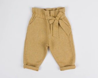 May include: Mustard yellow trousers with a bow tie detail at the waist.