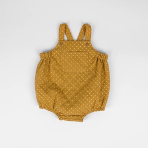 Pode incluir: Um macacão de bebê amarelo mostarda com bolinhas brancas e um pequeno bolso. O macacão tem alças e é acolchoado.