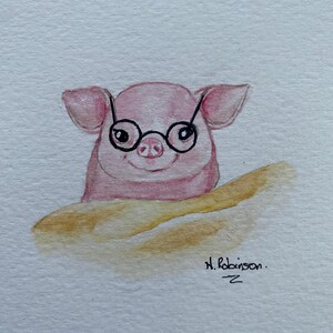 以下が含まれることがあります： 丸い黒いメガネをかけたピンク色の豚が、金茶色のバゲットの上からのぞいている水彩画。豚は笑顔です。署名「N. Robinson」と下に小さな「Z」があります。