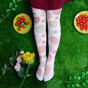 May include: Burgundy skirt and red sweater with a strawberry design. White tights patterned with pink and green apples, strawberries, and swirls. Yellow plates with strawberries and cherries on a green surface.