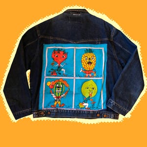 May include: A dark blue denim jacket with a colorful patch featuring cartoon fruits. The patch has a blue background with a strawberry, pineapple, watermelon, and lime. Each fruit has a face and is wearing clothes.