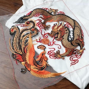 May include: A large embroidered patch featuring a golden dragon and a vibrant orange phoenix facing each other on a sheer white mesh fabric. The detailed design includes red swirling clouds and a central circular motif, all stitched with metallic thread.