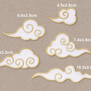 May include: Five white embroidered iron-on patches in the shape of clouds with gold outlines. The patches are different sizes, ranging from 4.5 x 2.8 cm to 10.5 x 2.8 cm. Each patch has a unique design of swirling clouds.