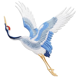 May include: A blue and white embroidered crane with outstretched wings. The crane is flying with its head turned to the left. The crane has a long, thin beak and long, thin legs.