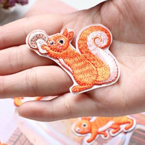 Puede incluir: Parche de hierro bordado de color naranja y blanco de una ardilla sosteniendo un hongo.