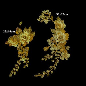 May include: Two gold embroidered floral appliques featuring intricate rose and leaf designs. The left applique measures 26x15cm, while the right elongated floral arrangement measures 38x12cm. Both pieces feature metallic gold thread detailing.