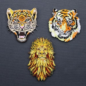 May include: Three embroidered iron-on patches featuring the faces of a lion, a tiger, and a leopard. The patches are all yellow, orange, and black.