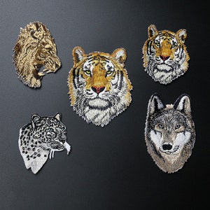 May include: Five embroidered iron-on patches featuring different animal faces. The patches include a lion, two tigers, a leopard, and a wolf. The patches are all in shades of brown, black, white, and yellow.