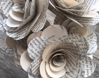 May include: A bouquet of three paper flowers made from the pages of old books. The flowers are white and cream colored and have a delicate, vintage look.