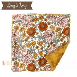 May include: A mustard yellow and white floral baby blanket with a soft, plush texture. The blanket features a vintage floral pattern with pink, orange, and blue flowers. The blanket is perfect for cuddling and comforting a baby.
