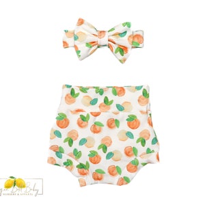 May include: White baby bloomers with a peach print. The bloomers have a white bow headband with a peach print.