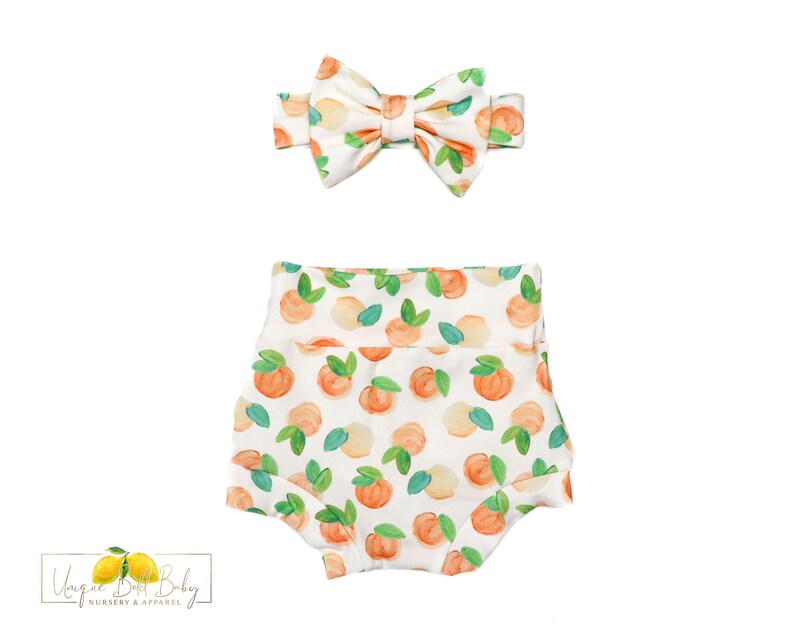 May include: White baby bloomers with a peach print. The bloomers have a white bow headband with a peach print.