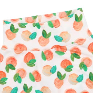 May include: White turtleneck top with a peach print. The peaches are painted in shades of orange, pink, and yellow with green leaves.
