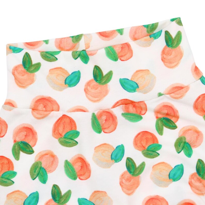 May include: White turtleneck top with a peach print. The peaches are painted in shades of orange, pink, and yellow with green leaves.