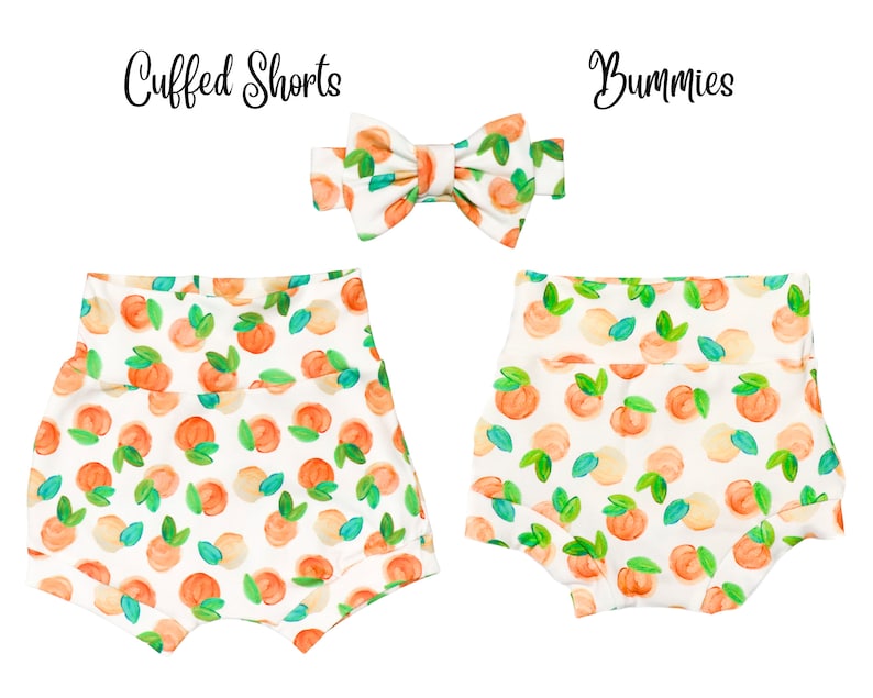 May include: A set of two peach-print baby clothes, including a pair of cuffed shorts and a bow. The shorts have a white background with peach and green watercolor-style illustrations. The bow is white with peach and green watercolor-style illustrations.