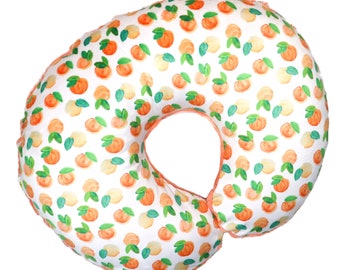 May include: A white and peach-colored pregnancy pillow with a peach and green pattern. The pillow is shaped like a donut and has a hole in the middle.
