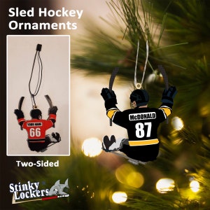 May include: Two-sided Christmas ornament featuring a hockey player on a sled. One side has the name "MCDONALD" and the number "87" on the jersey. The other side has the text "YOUR NAME" and the number "66" on the jersey.