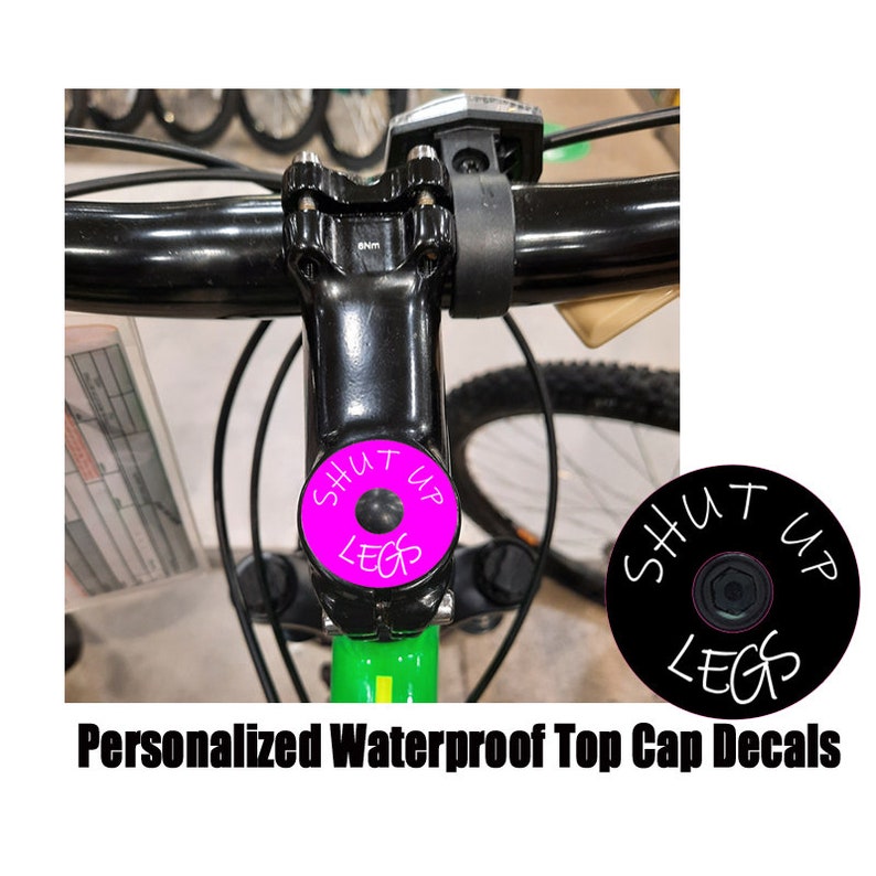 May include: A close-up of a black bicycle with a pink and white top cap decal that says "Shut Up Legs".