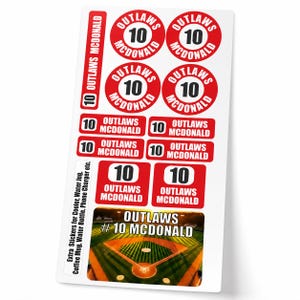 May include: A sheet of stickers featuring the text "OUTLAWS MCDONALD" and the number "10" in red and white. The stickers are in various shapes, including circles and rectangles. A baseball field graphic is also included.