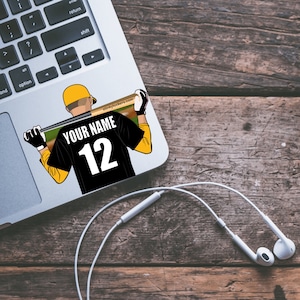 Peut inclure: Un maillot de baseball noir et jaune avec le texte "YOUR NAME" et le numéro "12" au dos. Le maillot est porté par un personnage de dessin animé tenant une batte de baseball.