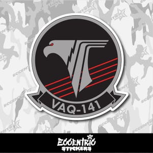 May include: A circular sticker featuring a stylized eagle head and a 'T' shape in gray, with red stripes and the text 'VAQ-141'. The design is set against a black background within a gray border.