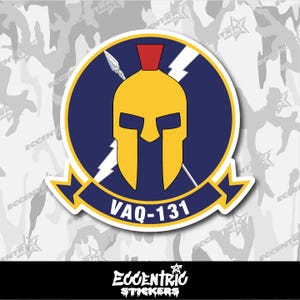 May include: A sticker featuring a yellow Spartan helmet with a red crest, set against a blue circle with lightning bolts. The text "VAQ-131" is displayed on a banner below the helmet. The sticker has a white border.