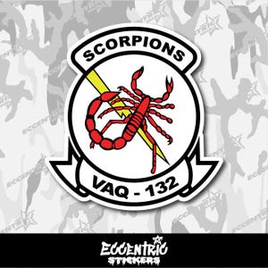 May include: A white sticker featuring a red scorpion design with yellow lightning bolts. The text "SCORPIONS" is arched above the scorpion, and "VAQ - 132" is below. The sticker has a black border and is on a camouflage background.