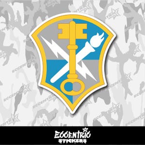 May include: A sticker featuring a shield design with a gold key, white torch, and lightning bolts on a blue and gray background. The sticker has a yellow border and the text "ECCENTRIC STICKERS" at the bottom.