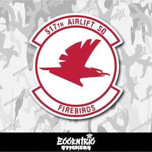 May include: A red and white sticker featuring the 517th Airlift Squadron emblem. The emblem includes a red bird silhouette within a white circle, with the words "517th Airlift SQ" and "FIREBIRDS" in red. The sticker has a white border.