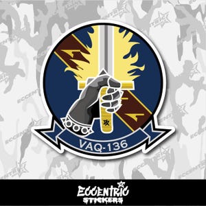 May include: A circular sticker featuring a stylized emblem. A black gloved hand firmly grips a yellow sword against a blue background. The text "VAQ-136" is displayed on a banner below. The sticker has a white border.