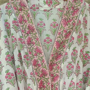 May include: White cotton robe with a pink and green floral print. The robe has a shawl collar and a tie belt.