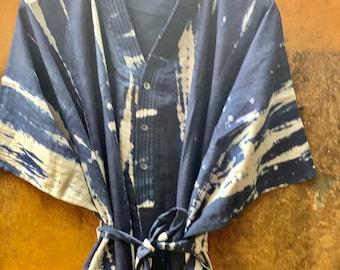 May include: A blue and white tie-dye cotton tunic with a V-neck and a button closure. The tunic has a tie belt and short sleeves.
