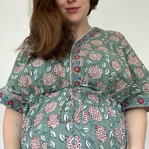 May include: A green, floral print kaftan with a V-neckline and short sleeves. The kaftan has a cinched waist and a flowing skirt.